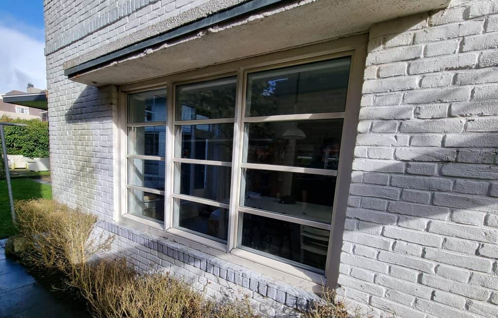 Nieuwe witte kunststof raamkozijnen met verduisteringslamellen, geïnstalleerd in een gevel van bakstenen gevel.