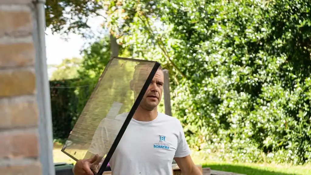 Glaszetter die een beschermend raam inzet op een raam in de tuin, buiten tijdens daglicht, onderhoud en glasservice Bonn, professioneel vakwerk.